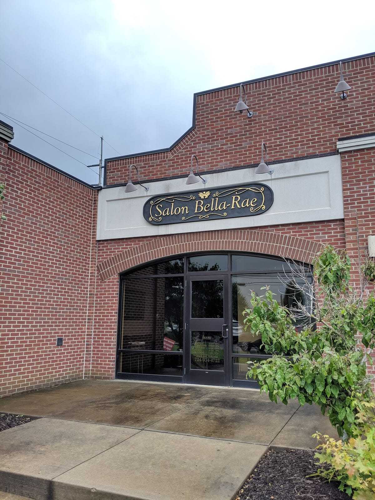 Brick building with "Salon Bella-Rae" sign above a glass door entrance on a rainy day.