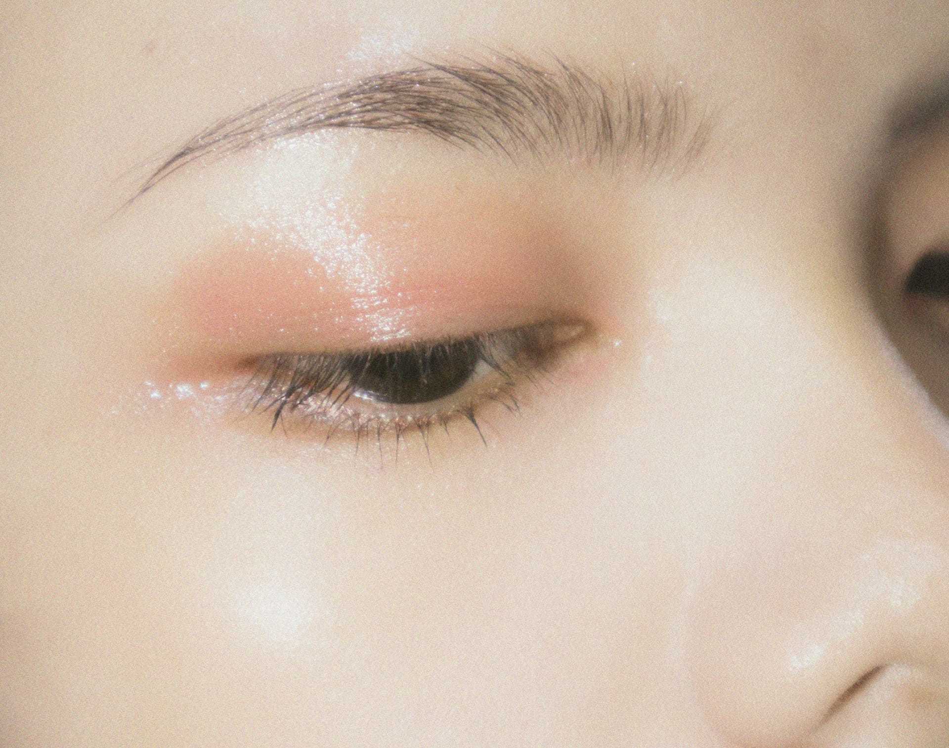 Soft makeup on a closed eye with shiny peach eyeshadow and groomed eyebrow.