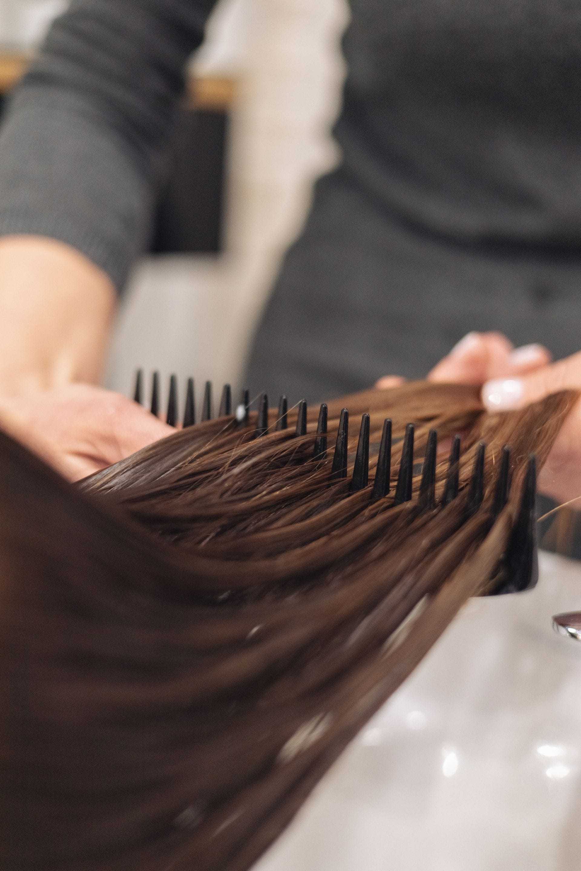 Hair being combed with a round brush by a person in a gray sweater.