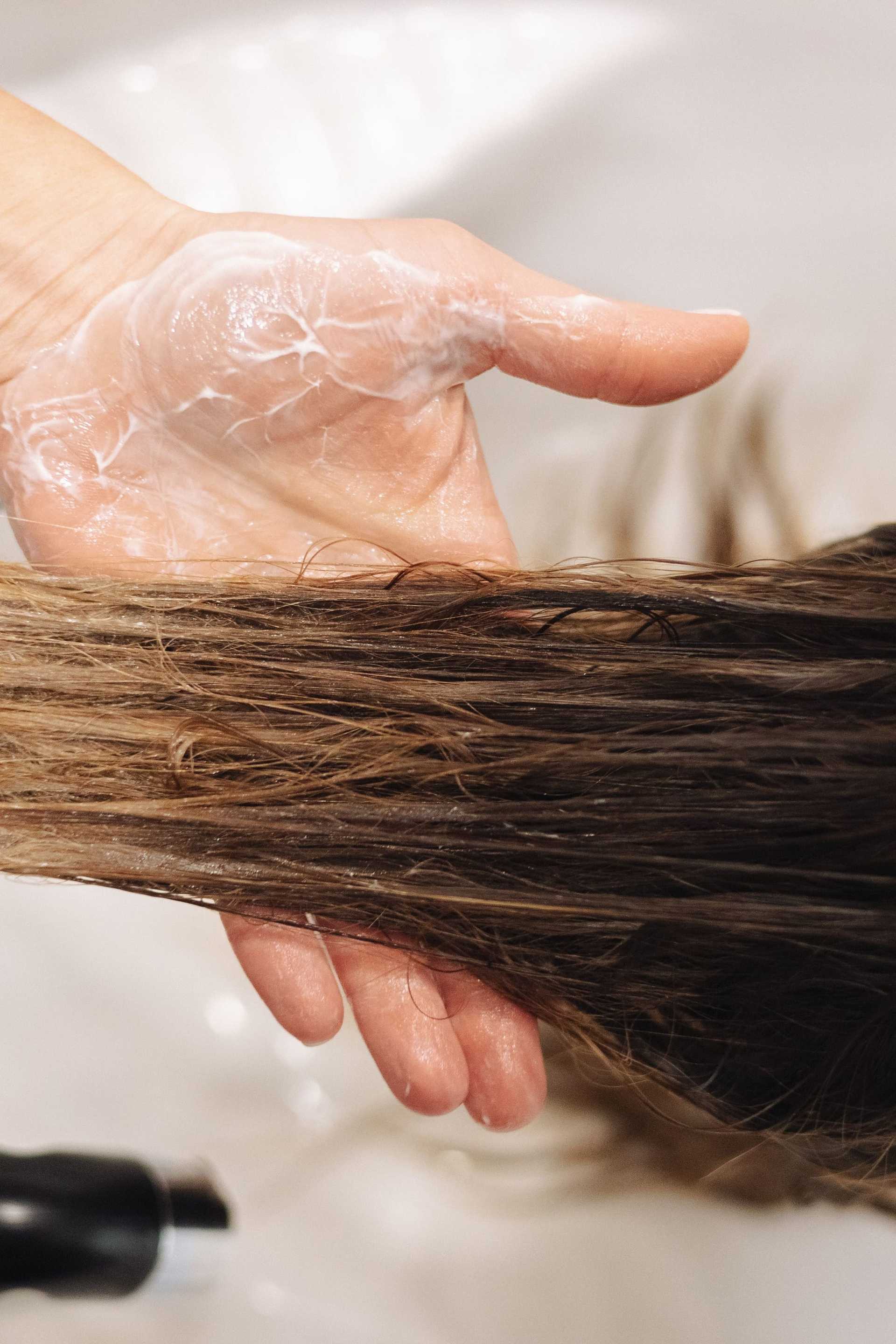 Applying conditioner to wet brown hair in a salon setting.