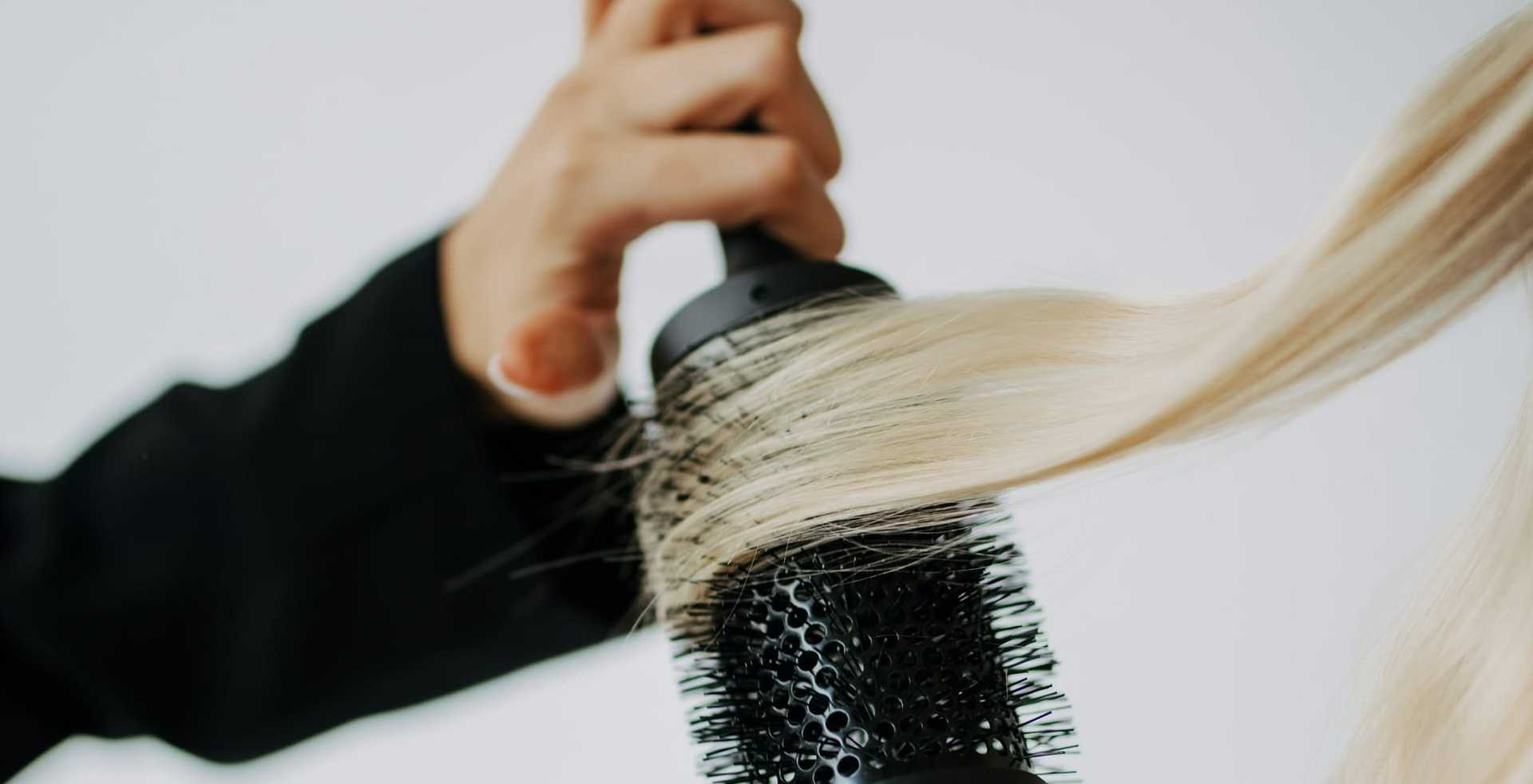 Person styling long, blonde hair with a round brush.