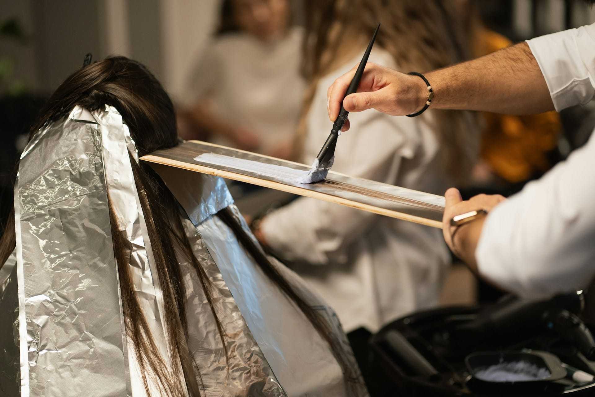 Hairdresser applying color to a client's hair with foil and brush.