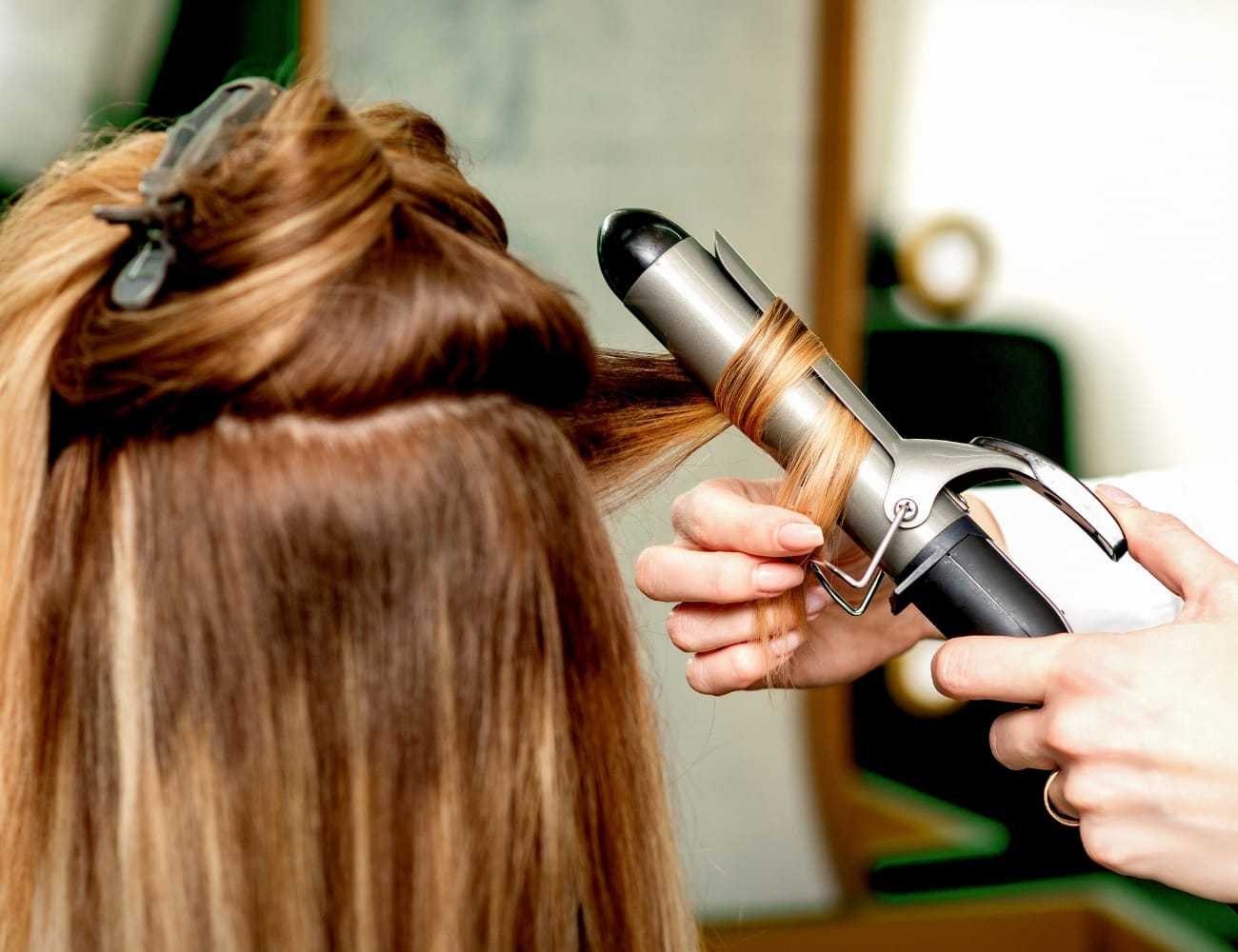 Hair stylist curling client's hair with a curling iron in a salon setting.